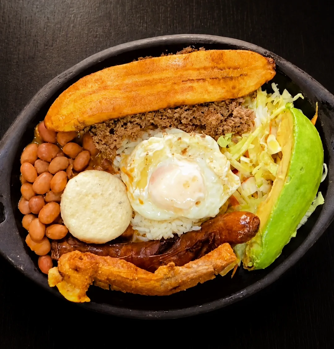 Bandeja paisa de Ricomilones vista desde arriba: plátano maduro, carne molida, fríjoles, arroz, huevo frito, arepa, chorizo, chicharrón y aguacate