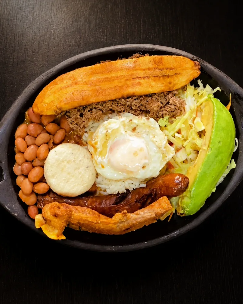 Bandeja paisa de Ricomilones vista desde arriba: plátano maduro, carne molida, fríjoles, arroz, huevo frito, arepa, chorizo, chicharrón y aguacate